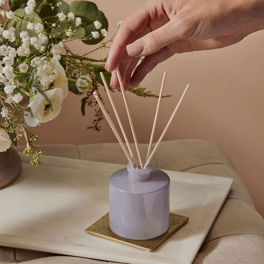 Setting up a Thymes Lavender Petite Reed Diffuser near vase of flowers image number 2